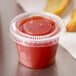 A Dart clear plastic souffle cup filled with red sauce.