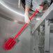 A person in gloves using a red Carlisle Sparta multi-purpose cleaning brush.