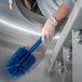 A person in gloves using a Carlisle blue brush with 5" bristles to clean a metal surface.