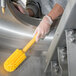 A person using a Carlisle yellow Sparta cleaning brush with a 3" bristle diameter to clean a machine.