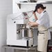 A woman in a white apron using an Estella spiral dough mixer to mix dough on a counter.