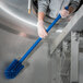 A person in gloves using a Carlisle blue brush with a blue handle to clean a stainless steel sink.