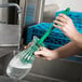 A person holding a Carlisle green bottle cleaning brush with a green handle.