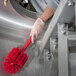 A person in gloves holding a red Carlisle Sparta multi-purpose cleaning brush.
