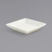 A white square porcelain sauce dish with a lid on a gray surface.