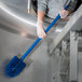A person in gloves cleaning a stainless steel sink with a blue Carlisle Sparta brush.