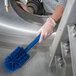 A person in gloves cleaning a metal surface with a blue Carlisle Sparta brush.