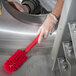 A person in gloves using a Carlisle red brush with a red handle to clean a metal surface.