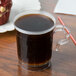 A clear plastic WNA Comet coffee cup filled with coffee on a table.