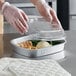 A person in gloves holding a plastic lid over a ChoiceHD Smoothwall Silver large foil tray of food.