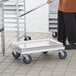 A man pushing a Regency aluminum bun pan dolly with a tray on top.