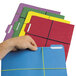 A person's hand holding a file folder with colorful papers using a blue rubber band.
