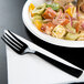 A black WNA Comet Classicware EcoSense plastic fork next to a plate of pasta and tortellini.