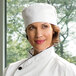 A woman wearing a white Uncommon Chef skull cap in a professional kitchen.