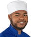 A smiling black man wearing a white Uncommon Chef skull cap in a professional kitchen.