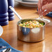 A hand holding a Vollrath mini stainless steel sauce pan with macaroni and cheese and a spoon.