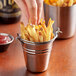 A person holding a Vollrath mini stainless steel bucket of french fries.