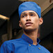 A man wearing a Uncommon Chef royal blue hat and jacket standing in a professional kitchen.