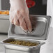 A person in gloves using a Carlisle stainless steel steam table pan cover to seal a container of food.