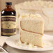 A slice of cake with white frosting next to a bottle of Nielsen-Massey Madagascar Bourbon Vanilla Extract.
