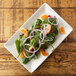 A rectangular white porcelain plate with a spinach salad with oranges and red onions.