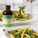 A plate of green beans with a bottle of Nielsen-Massey Organic Madagascar Bourbon Vanilla Extract on the side.