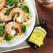 A bottle of Nielsen-Massey Pure Lemon Extract on a table with a plate of pasta with shrimp and broccoli.