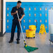 A man holding a Rubbermaid metal mop handle with a white jaw style attachment and mopping the floor.