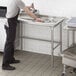 A man in a black apron standing next to a Regency stainless steel sorting table.