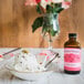 A bowl of ice cream with a spoon and a bottle of Nielsen-Massey Rose Water.
