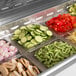A Turbo Air stainless steel refrigerated sandwich prep table with containers of vegetables and chopped tomatoes on a counter.