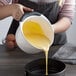 A woman using an OXO Good Grips white measuring cup to pour yellow liquid into a white bowl.