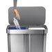 A hand reaching out to put a plastic bottle in a simplehuman dual compartment recycling bin.