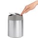 A hand opening a simplehuman brushed stainless steel countertop trash can.