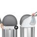 Two people use a simplehuman white plastic bag to line a trash can.