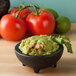 A Chico Molcajete filled with guacamole and tomatoes on a table.