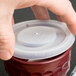 A hand placing a Dinex translucent plastic lid on a mug.