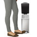A woman in grey pants using a simplehuman stainless steel rectangular end step-on trash can.