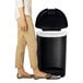 A woman standing next to a black simplehuman semi-round step-on trash can.