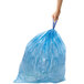 A hand holding a blue plastic bag with a box of simplehuman Code K blue recycling liners in the background.