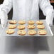 A person in a chef's uniform holding a Vollrath rimless aluminum cookie sheet with chocolate chip cookies.
