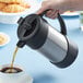 A hand using the stainless steel Thermos coffee press to pour coffee into a cup.