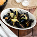 An ivory oval china platter with mussels and lemon wedges.