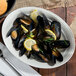 An ivory oval china platter with mussels, lemons, and rosemary.