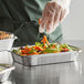 A person wearing plastic gloves placing carrots in a Choice foil take-out container of food.