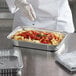 A chef preparing a tray of pasta in a Choice oblong foil container.