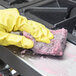 A person wearing yellow gloves cleaning a stove with a Scrubble steel wool soap pad.