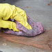 A person wearing yellow gloves cleaning wood with a Scrubble steel wool soap pad.