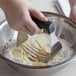 A hand holding a black OXO stainless steel pastry blender with 5 blades mixing butter in a bowl of flour.