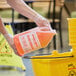 A person in gloves pouring Advantage Chemicals orange degreaser into a yellow container.